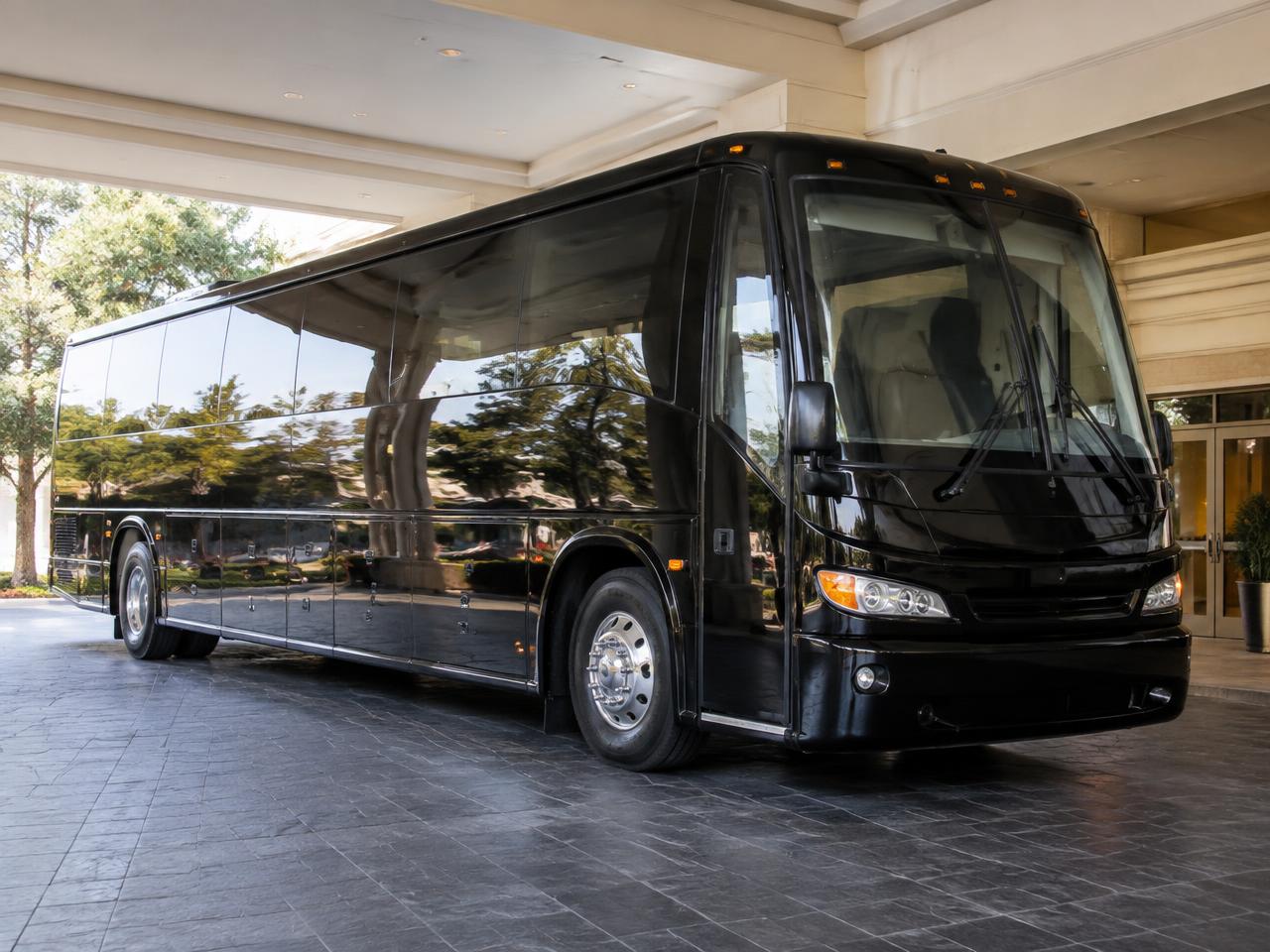 Black 37-passenger charter bus with luggage bays at a hotel